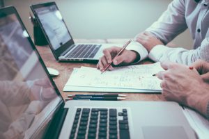 Dos personas revisando estrategia en papel con dos portátiles